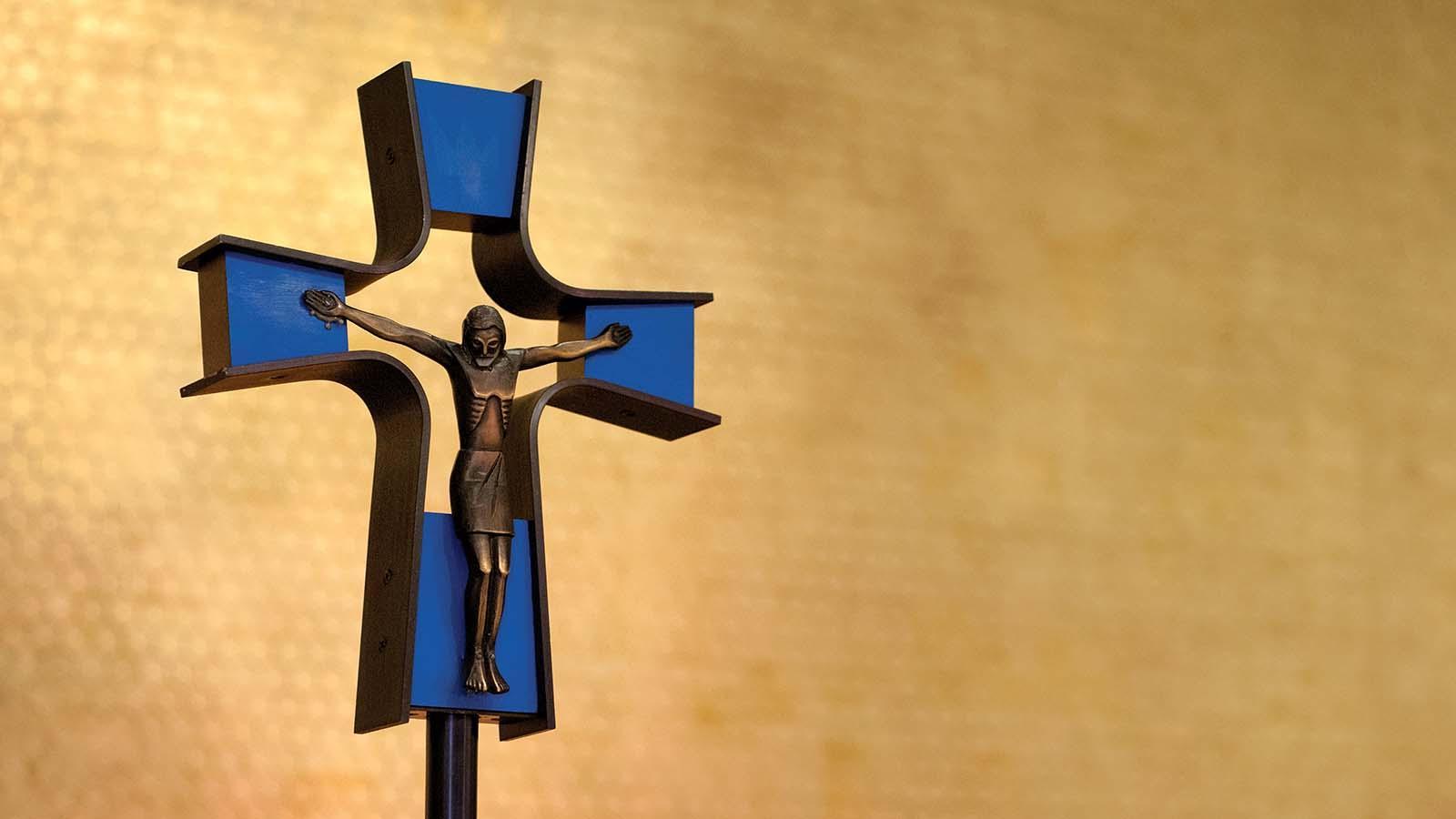 Closeup of crucifix in front of gold-leafed wall.